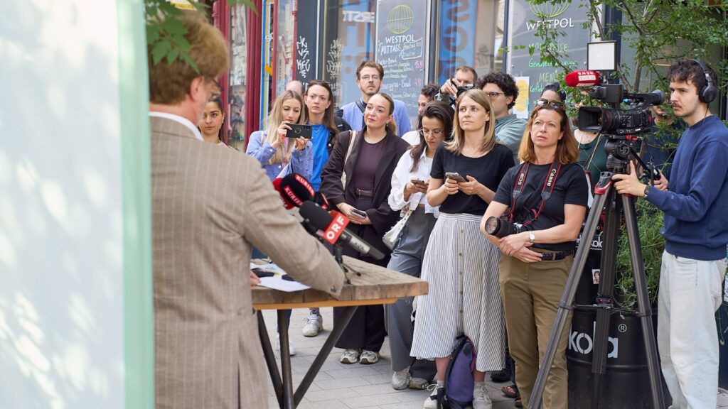 Medienvertreter:innen verfolgen die GOLIF-Pressekonferenz vor dem Restaurant Westpol in der Lerchenfelder Straße. ORF- und TV-Kameras dokumentieren die Veranstaltung.