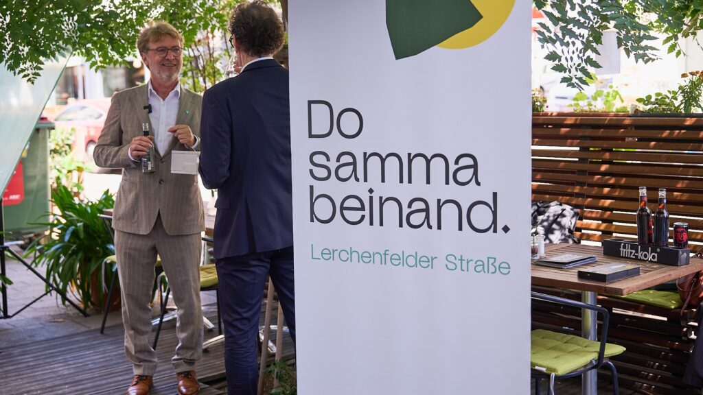 Markus Reiter und Martin Fabisch im Gespräch bei der GOLIF-Pressekonferenz vor dem „Do samma beinand.“-Banner in der Lerchenfelder Straße.