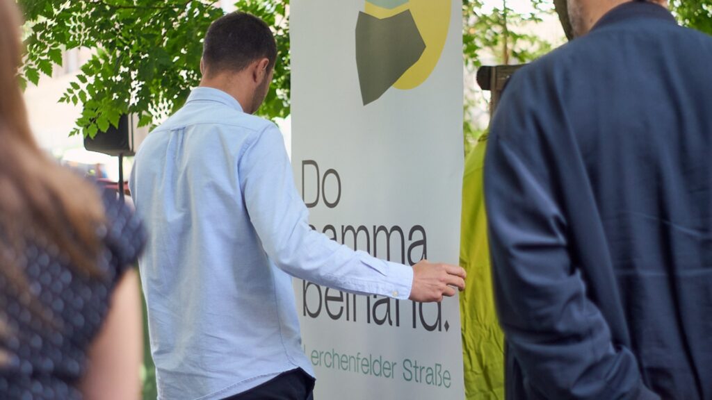 Besucher*innen bei der GOLIF-Pressekonferenz der IG Kaufleute Lerchenfelder Straße vor einem „Do samma beinand.“-Banner.