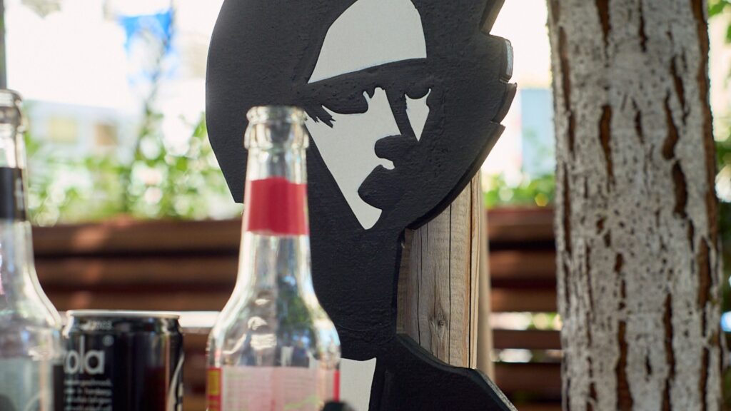 Detailaufnahme einer GOLIF-Pfandkellner*innen-Figur aus Holz mit Pfandflaschen und Getränkedose im Vordergrund.